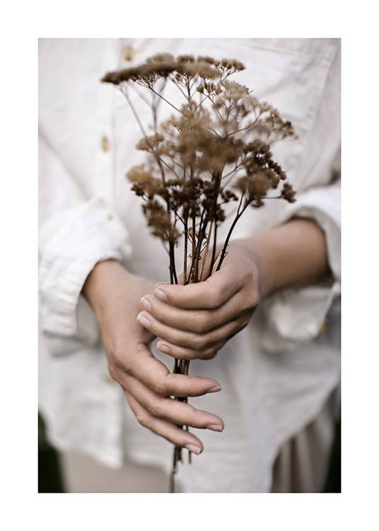  – Fotografia de uma mulher a segurar um bouquet com flores secas, tendo a sua camisa em linho branco como fundo