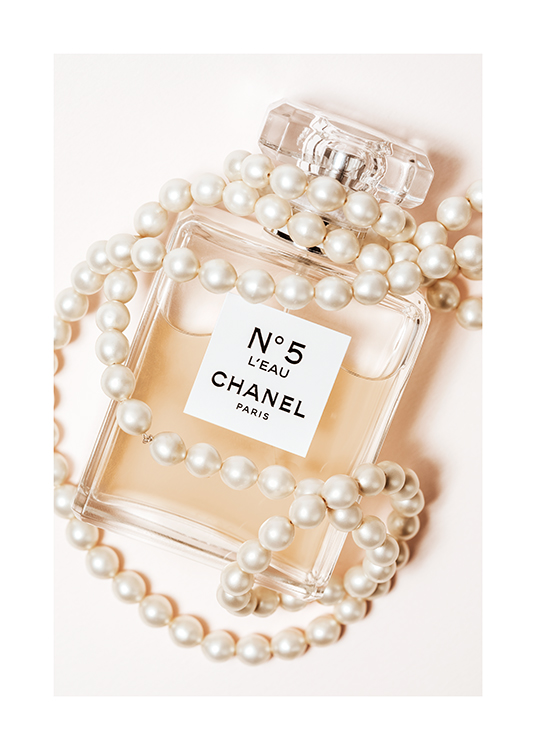  – Fotografia de um frasco de perfume Chanel No5 encolto em pérolas sob um fundo bege claro