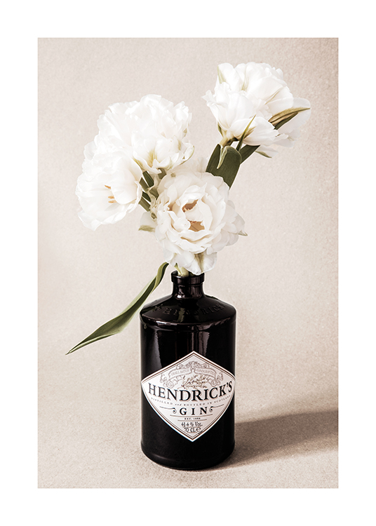  – Fotografia de um ramo de flores brancas numa garrafa de gim preta contra um fundo bege granulado